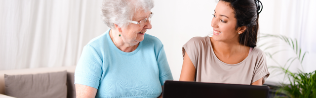 A young women sits with an older woman and helps her use a laptop