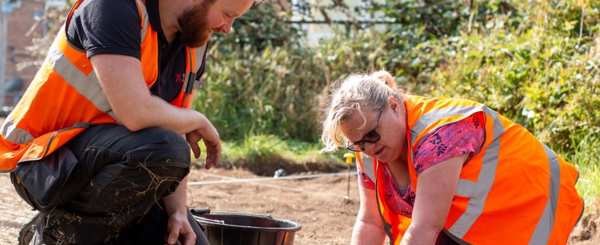 A man and woman in high vis look at the ground during a dig