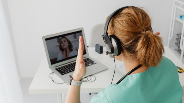 A healthcare professional sitting wearing headphones and speaking with someone over video call