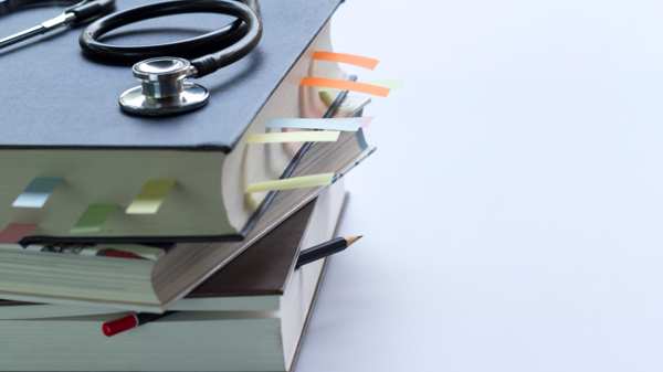 A stethoscope placed on top of large medical textbooks